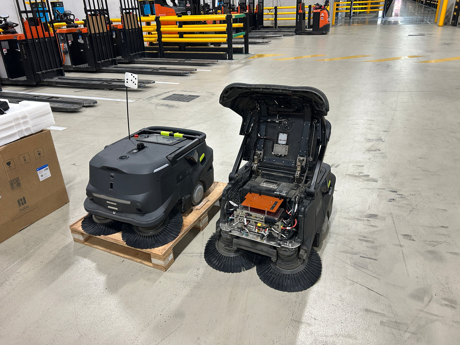 two MT1 Sweeping Robots on a warehouse floor with boxes and equipment in the background From Robot Solutions QLD