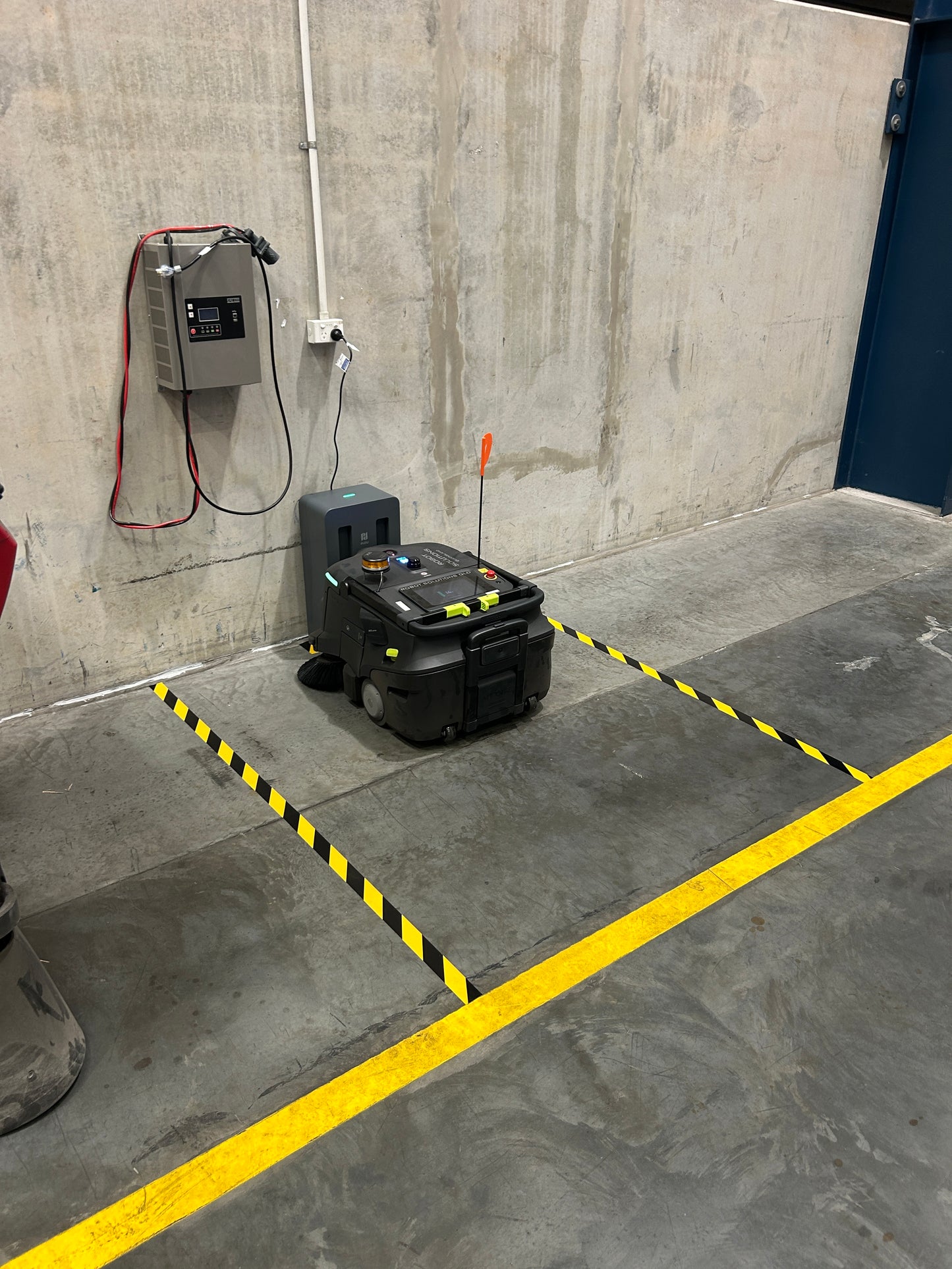 Sweeping robot on a concrete floor with yellow and black striped warning tape. From Robot Solutions QLD