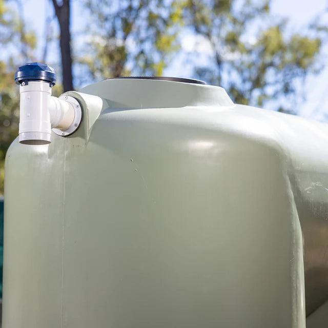 Large green water tank with a blue cap and white valve against a blurred natural background